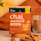 Box of Tea India Chai Moments Cinnamon instant chai tea latte with a glass of tea and cinnamon sticks on a warm background.