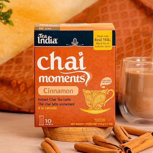 Box of Tea India Chai Moments Cinnamon instant chai tea latte with a glass of tea and cinnamon sticks on a warm background.