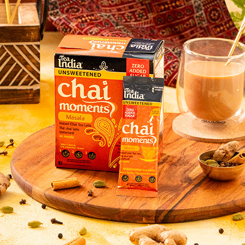 Tea India Chai Moments Masala Unsweetened No Sugar Added packaging on a wooden board with a glass of chai