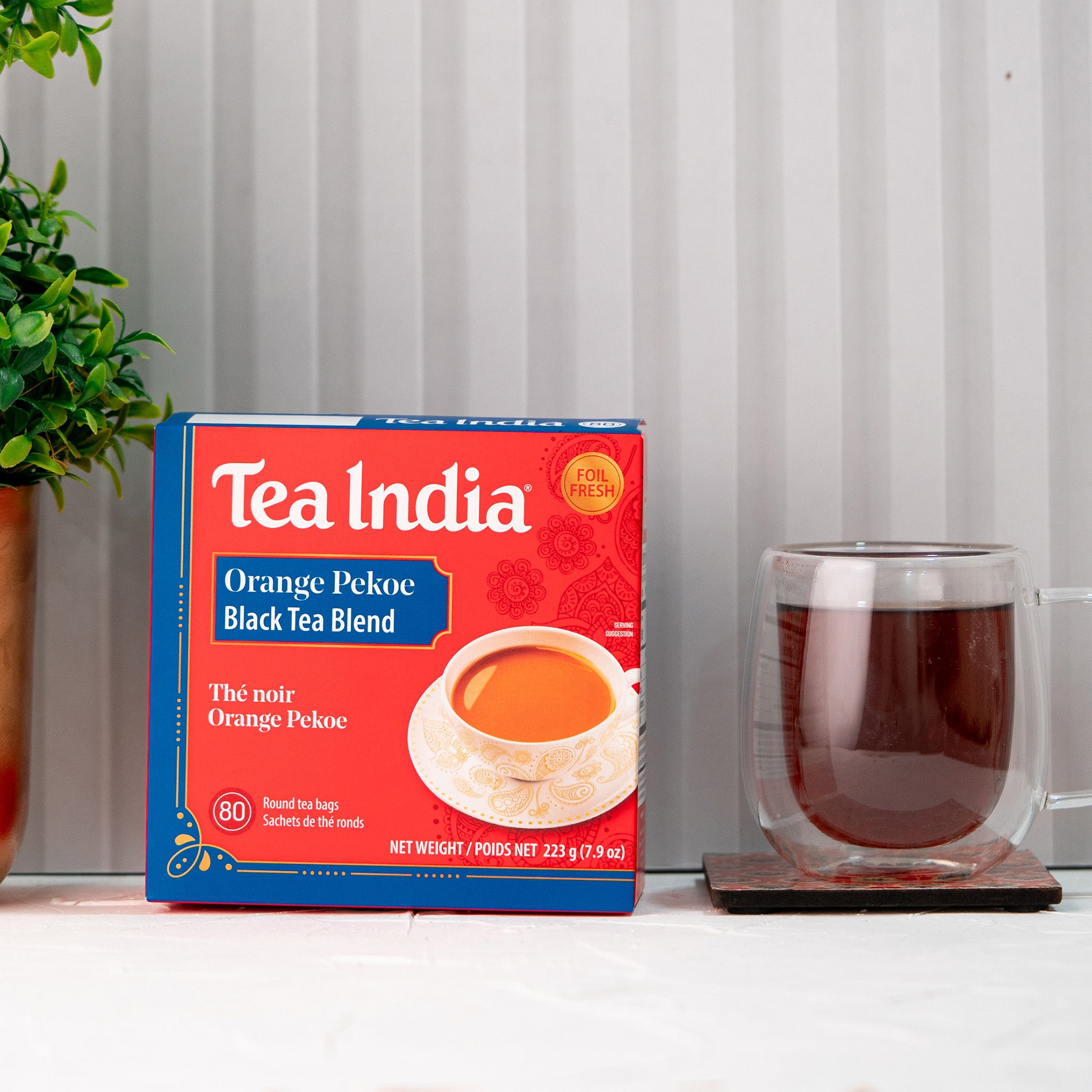 Box of Tea India Orange Pekoe Black Tea Blend with a cup of tea on a white surface.