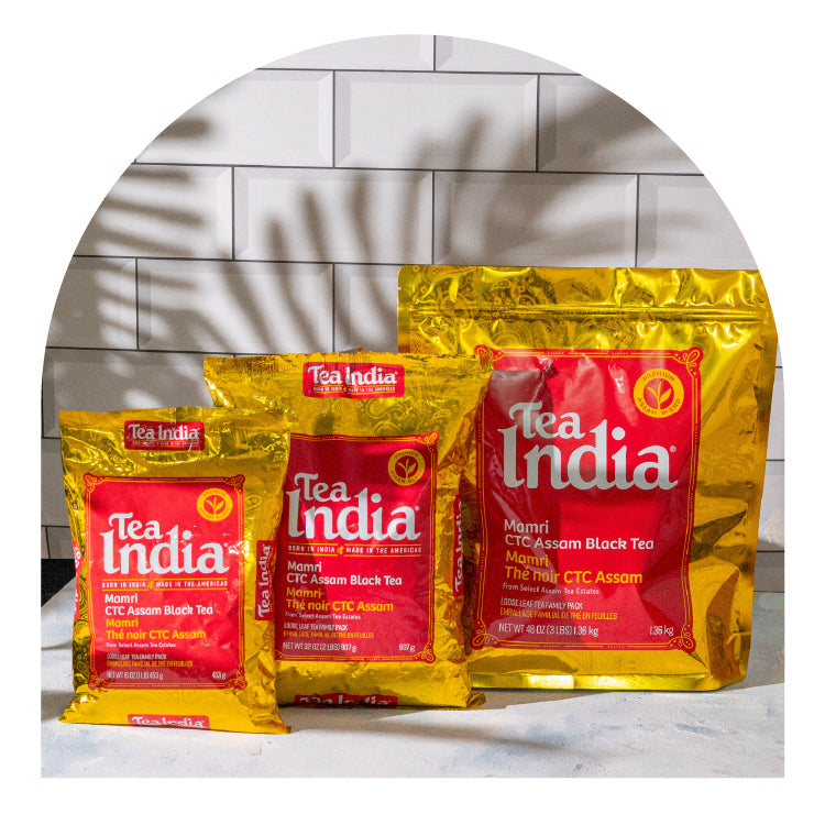 Three packages of Tea India tea on a white surface with a tiled wall background.