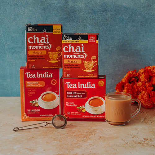 Tea India masala chai moments and masala black tea boxes with a cup of tea and a tea infuser on a wooden surface.