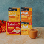 Tea India chai moments ginger tea boxes with a glass mug of tea on a wooden surface.