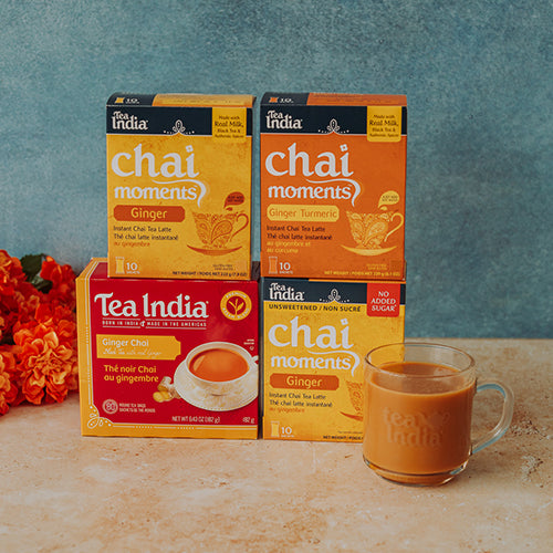 Tea India chai moments ginger tea boxes with a glass mug of tea on a wooden surface.