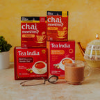 Tea India masala chai moments and masala black tea boxes with a cup of tea and a tea infuser on a wooden surface.