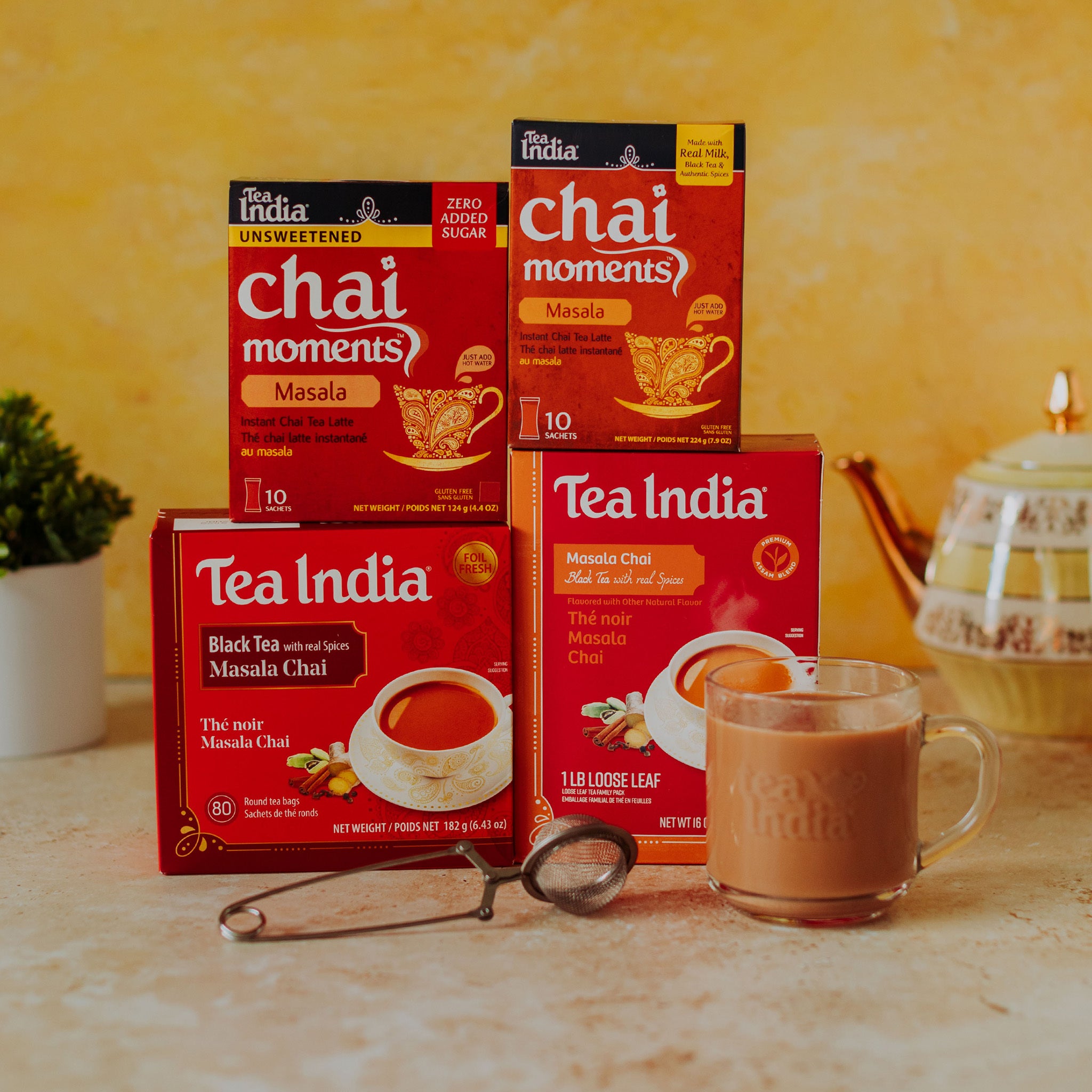 Tea India masala chai moments and masala black tea boxes with a cup of tea and a tea infuser on a wooden surface.