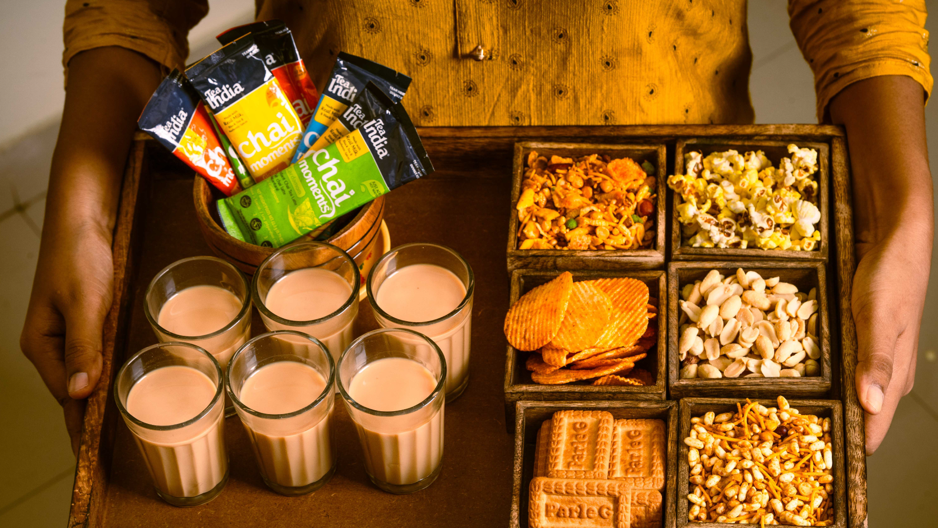 Assorted snacks including chips, popcorn, and drinks on a tray held by a person.