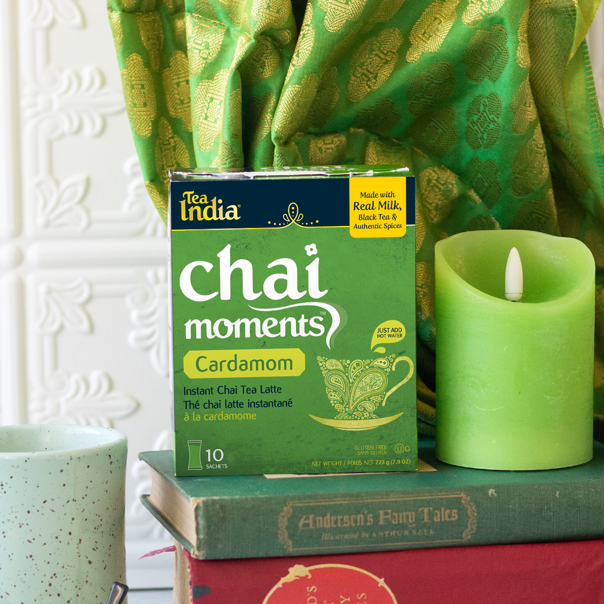 Tea India cardamom chai moments instant latte box with green candle, ceramic mug, and books in a cozy decorative setup