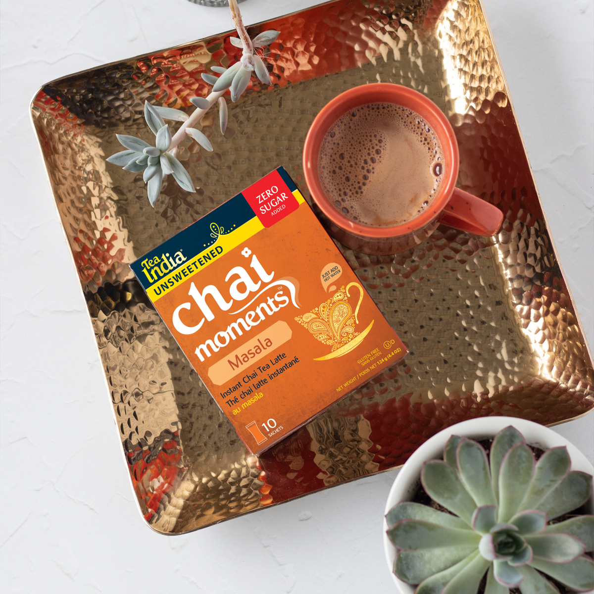 Box of Tea India Chai Moments Masala with a mug of chai latte on a gold tray next to succulents in a cozy setting