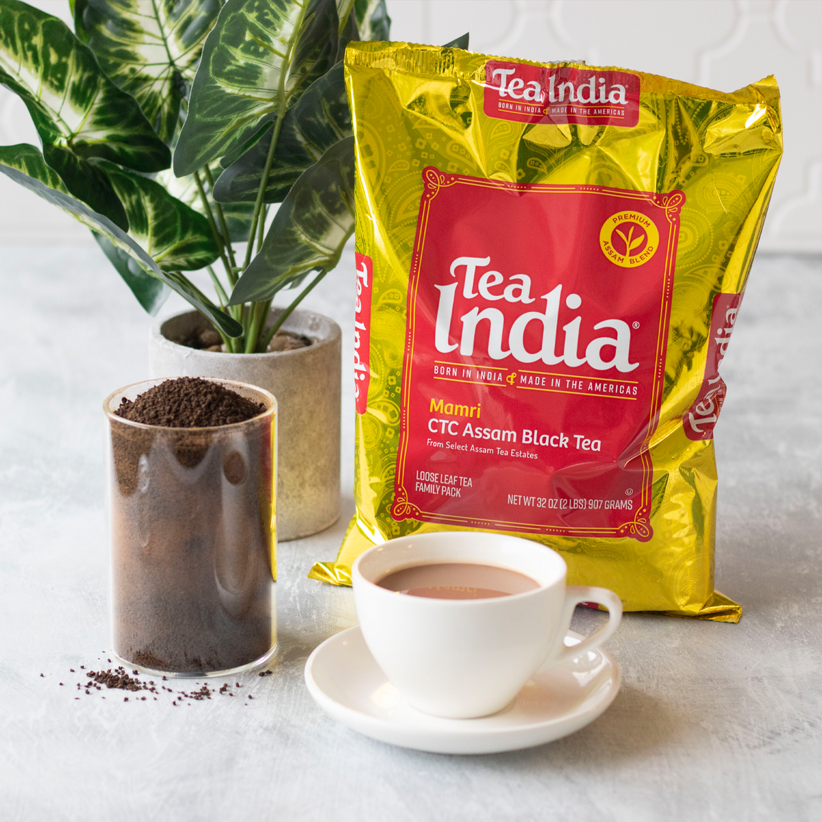 Bag of Tea India Mamri CTC Assam Black Tea with loose leaf tea, cup of chai, and green plant.